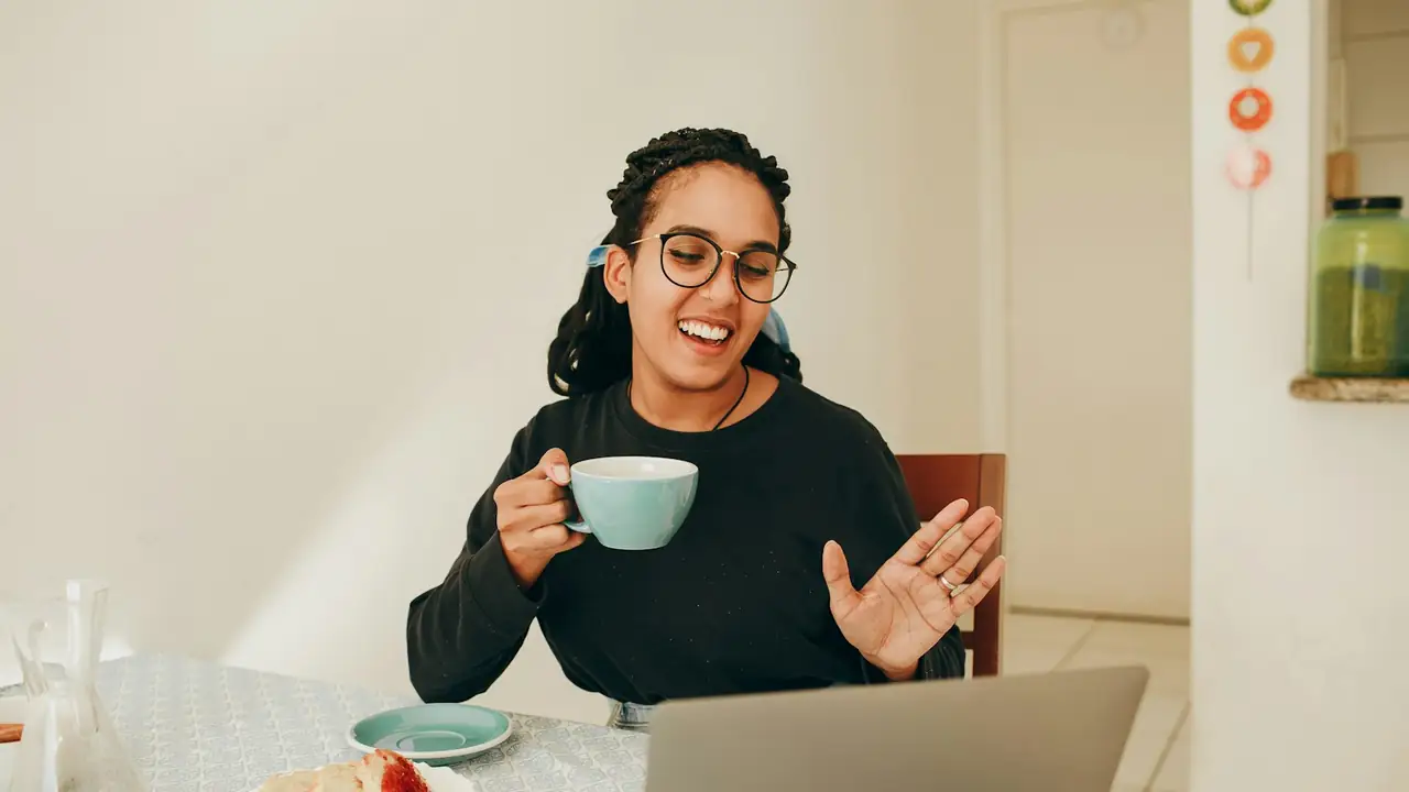 Consultante souriante en visioconférence, une tasse à la main