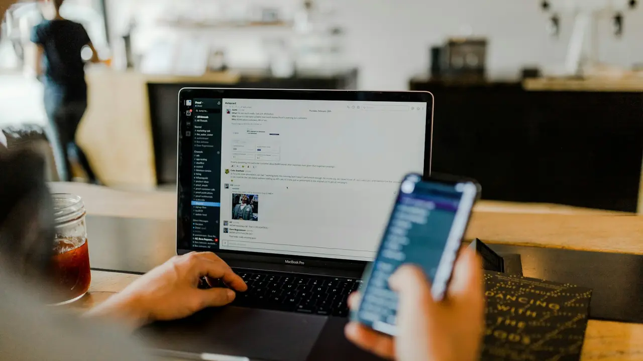 Personne qui consulte ses e-mails sur un téléphone, devant son ordinateur