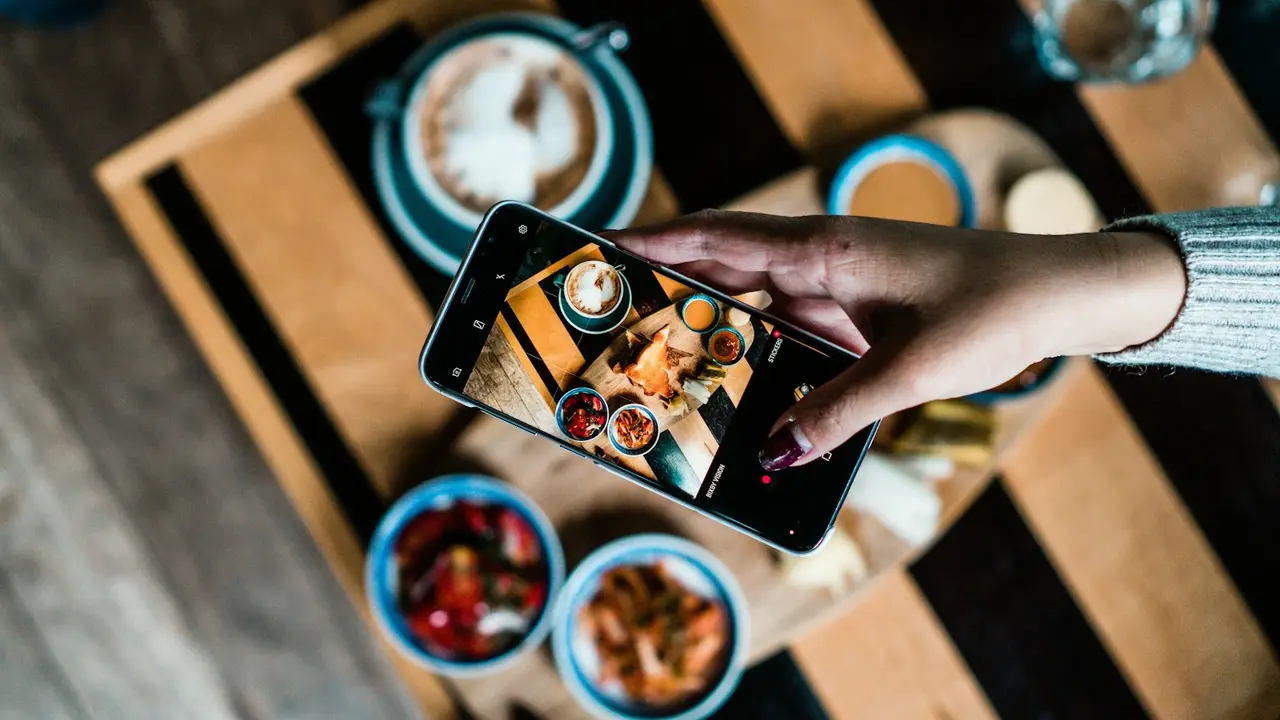 Main photographiant des plats au téléphone, vu de dessus